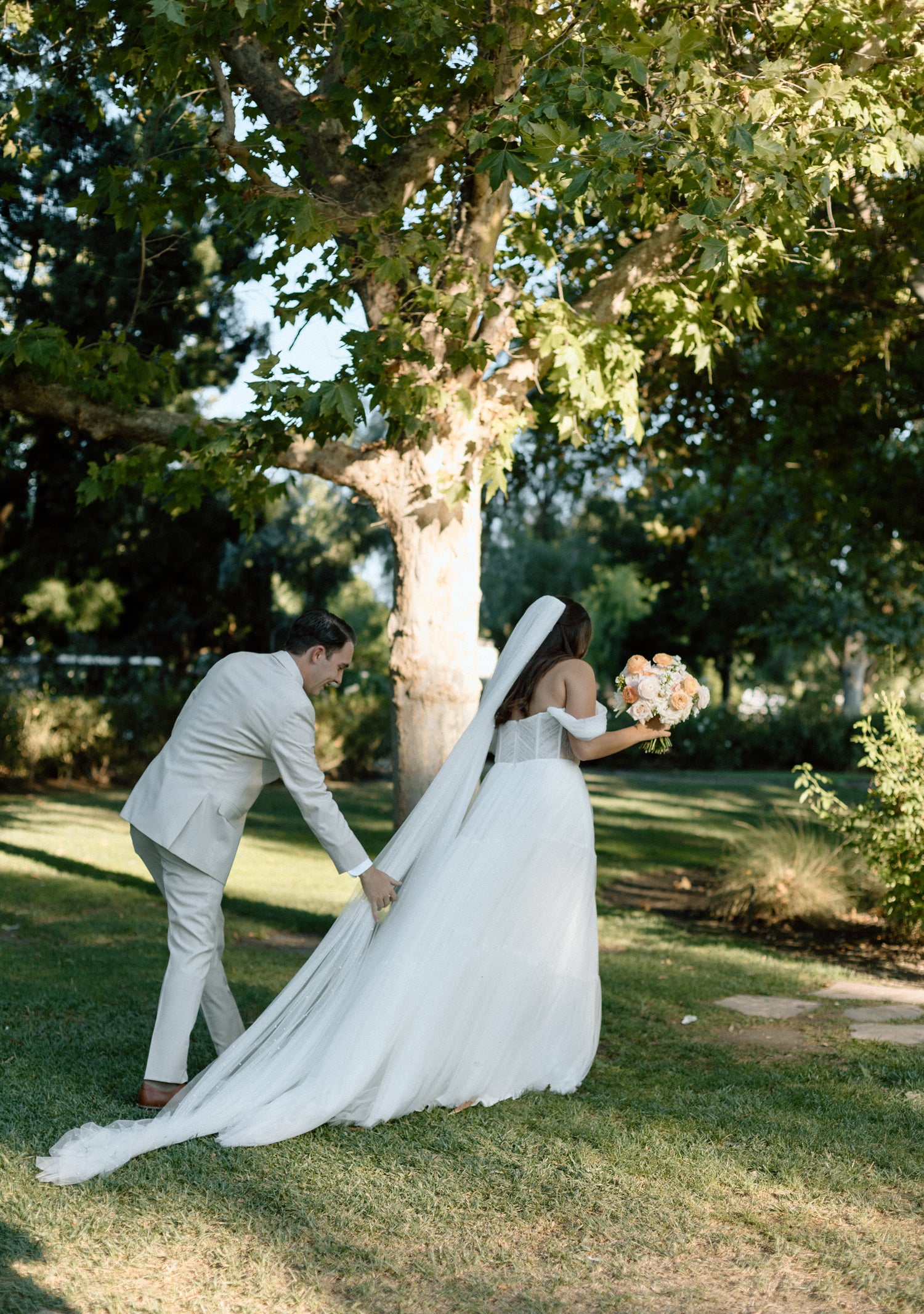 Bride and groom in a park with the bride's veil flowing.