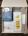 Comfort-focused period support box with tea, cookies, calming shower steamers, cloud socks, and a bath scrub displayed together on a textured background.