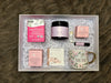 Gift box with various items including a mug, tea, and skincare products on a textured surface.