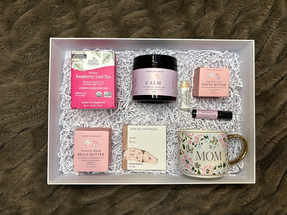 Gift box with various items including a mug, tea, and skincare products on a textured surface.